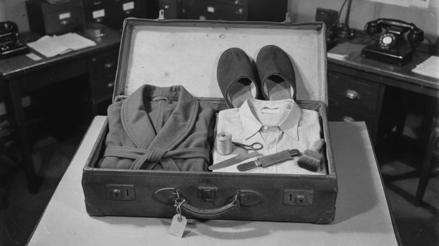 Reconstruction: an open leather suitcase with folded clothing, thread, scissors and a short knife
