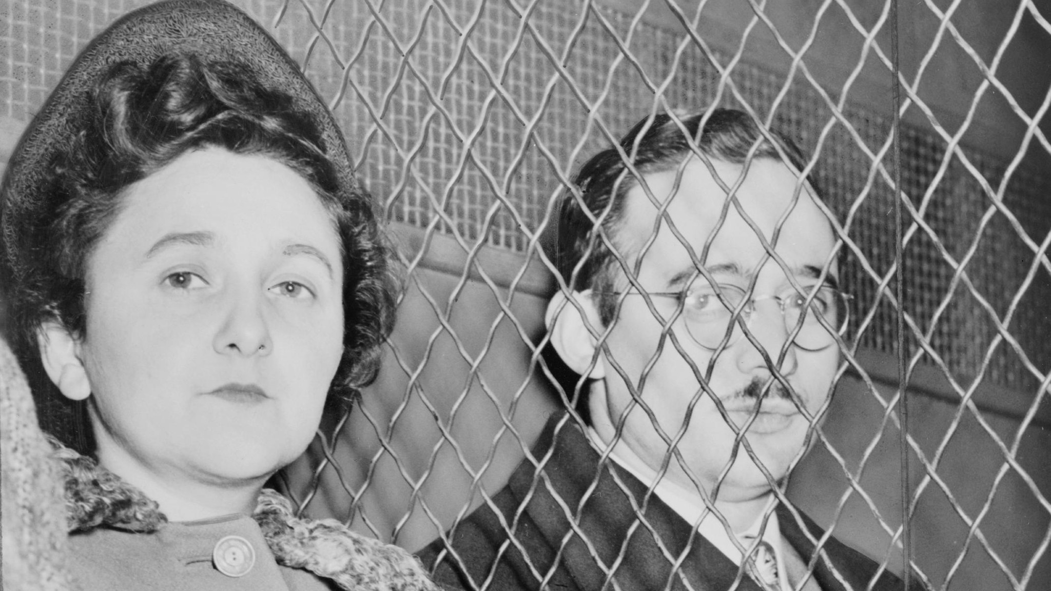 Archival photograph: Ethel and Julius Rosenberg side by side behind a wire-mesh screen
